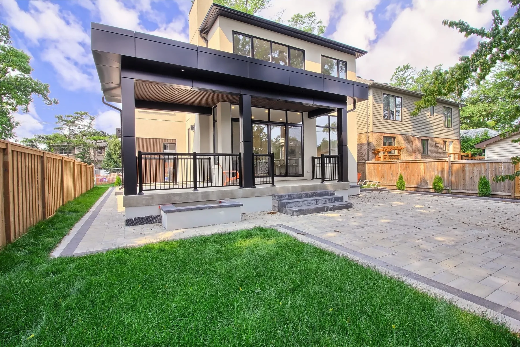 The rear of the house with a covered patio under a dark soffit, opening onto a paved terrace and lawn