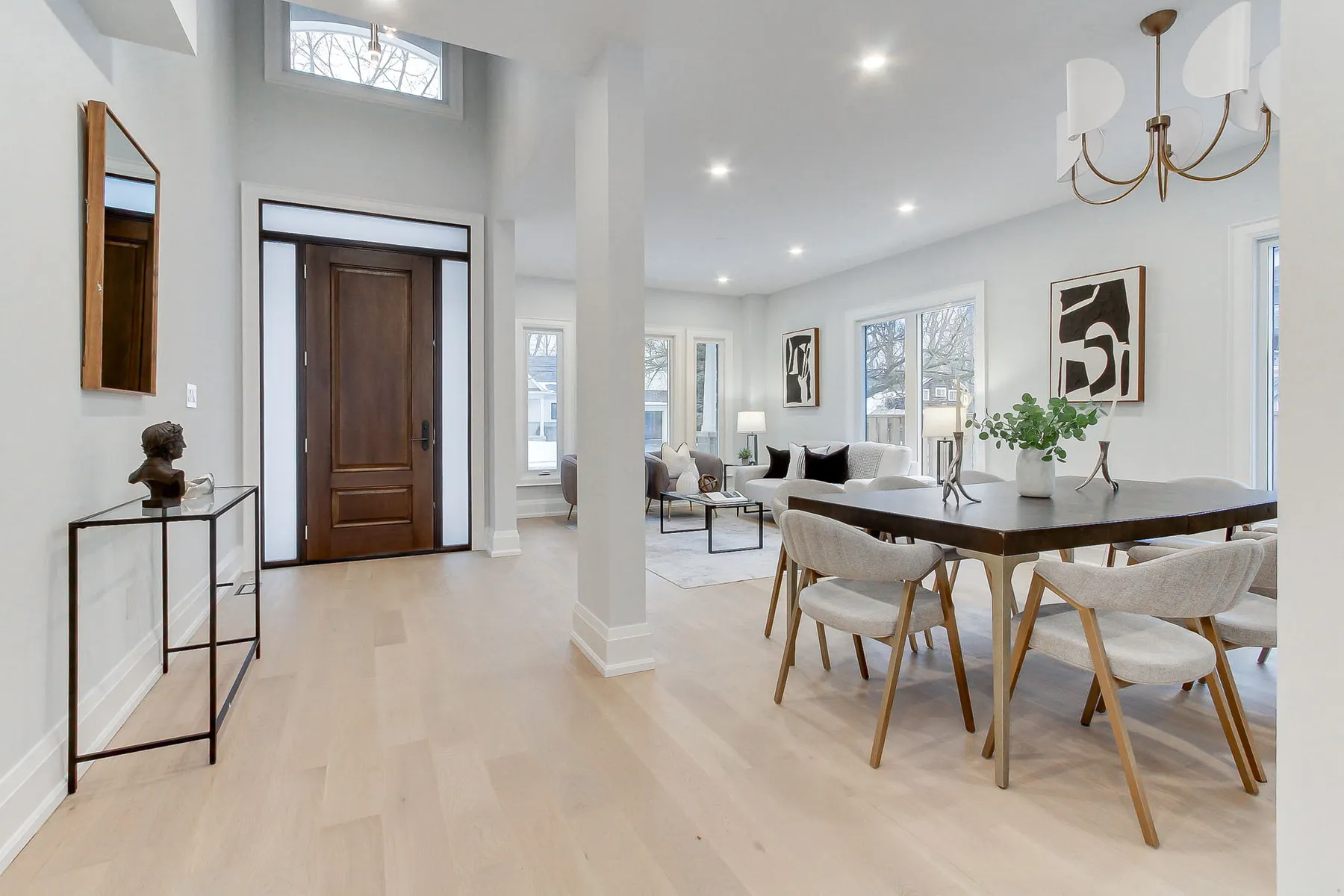A double-height foyer with a solid wood front door and transom, opening to a dining area on light oak floors