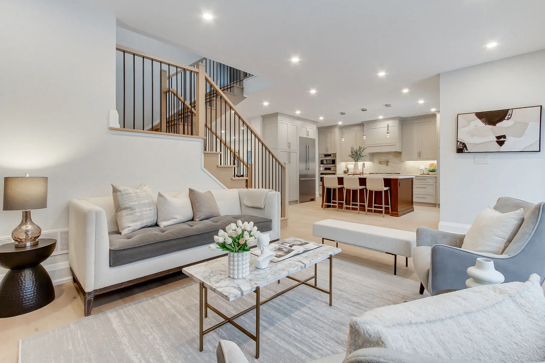 A living room with a cream sofa and marble coffee table, opening past the staircase to the kitchen beyond