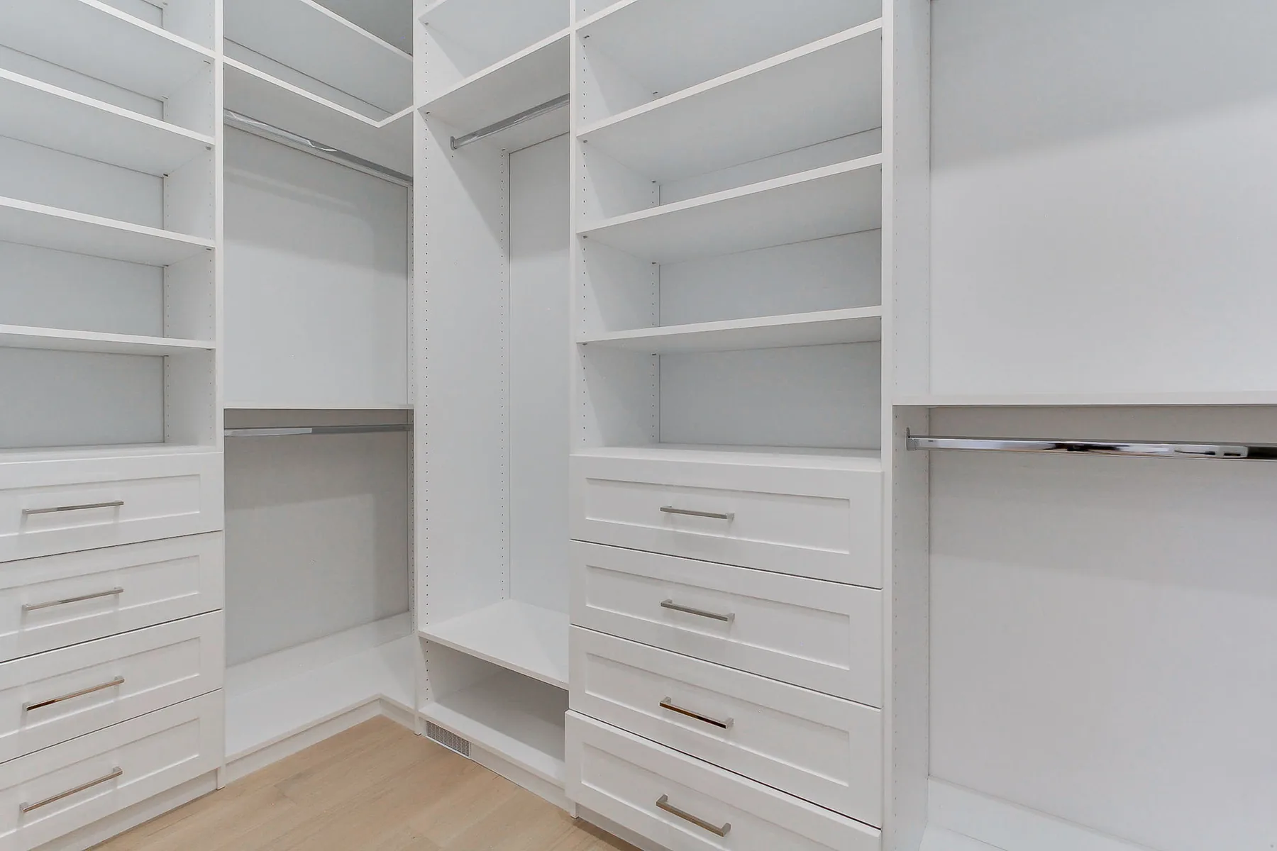 A walk-in closet fitted out in white built-in shelving, drawers and hanging rails